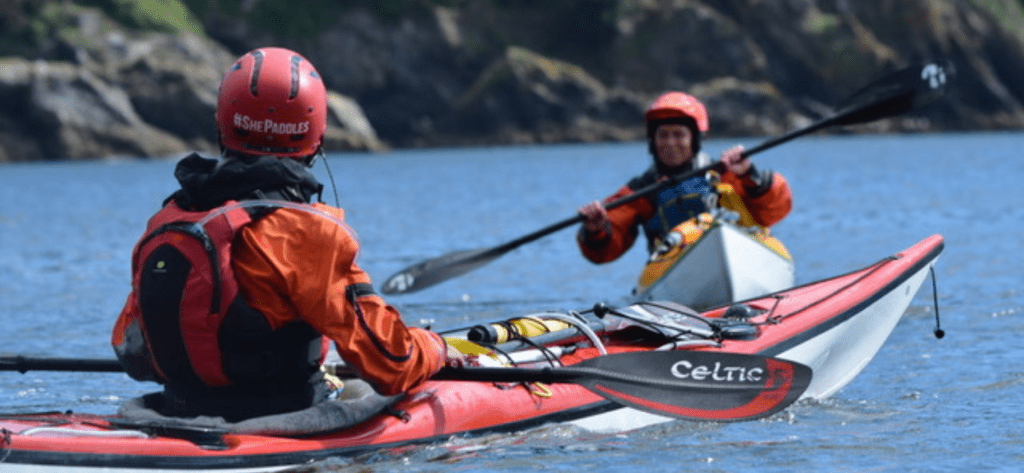 A close up of the back of one women sitting in her sea kayak as another female sea kayaker paddles towards her