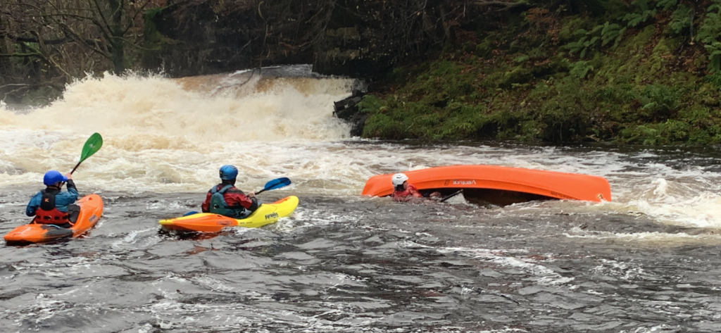 two kayakers rescuring an overturned canoe and paddler in the white water