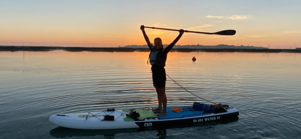 a girl on her stand up paddleboard, with the sunset in the background