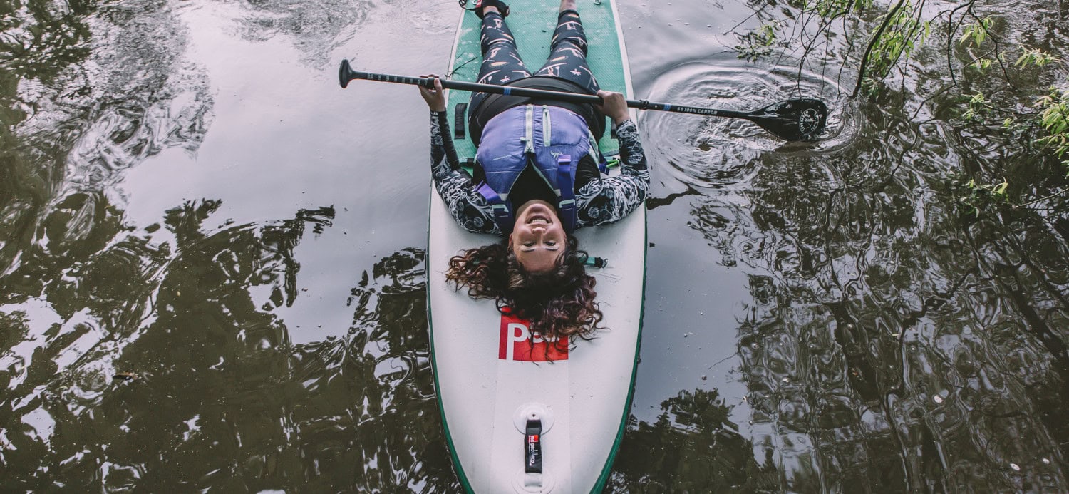 Natasha lying on her stand up paddleboard with her paddle