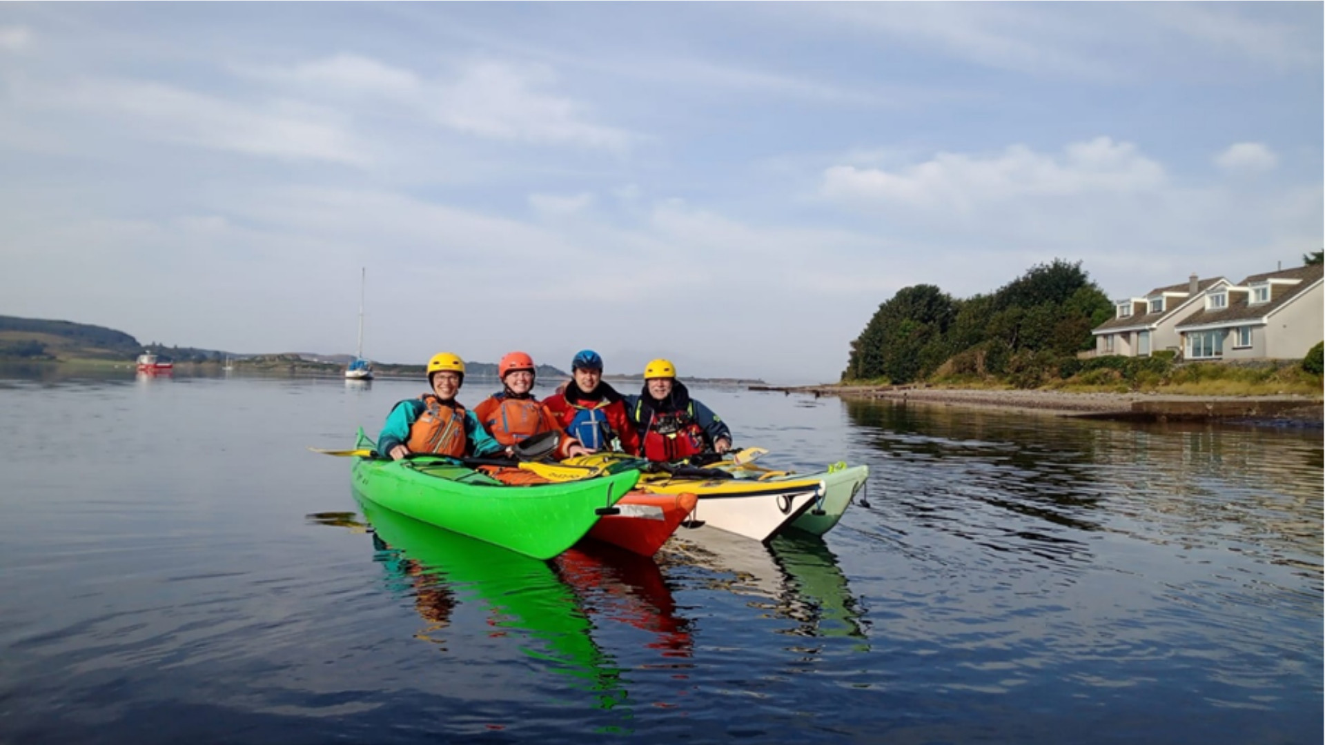 Image of Marianne, Kathleen, John and Rich posing together in their Sea Kayaks on calm flat water. 